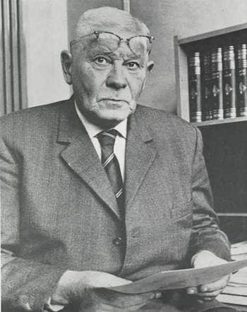 Willem Meiborg, streng kijkend, in een stug pak, papier in handen en bril net boven de ogen gezet